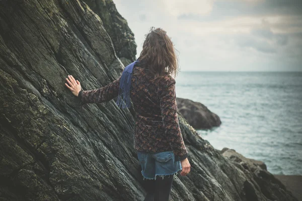 Young woman standing by a rock on the coast — Stock Photo, Image