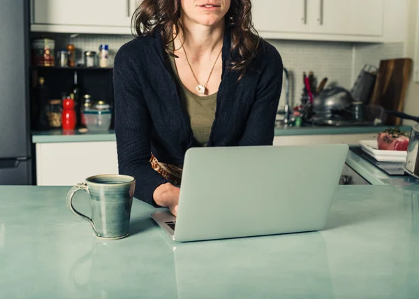 Mujer joven usando el ordenador portátil en la cocina —  Fotos de Stock