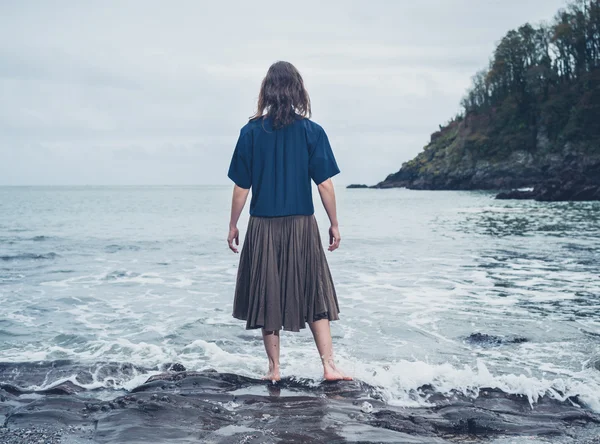 Young woman standing by the water on beach — Stock Photo, Image