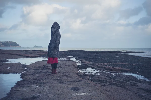 Jovem mulher de casaco com capuz andando na praia — Fotografia de Stock