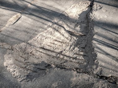 Delikleri ve çıkıntılı demir çubuğu olan bozuk bir yol. Yol yatağının tamir edilmesi gerekiyor.