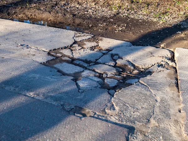 broken road with holes and protruding stones close-up, need for repair of the roadbed, cnfhst road, abandoned infrastructure