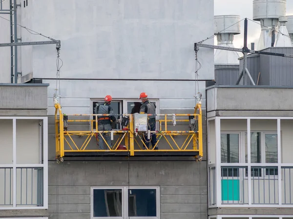 construction workers installers high-rise workers industrial climbers, painters on the lift paint the facade of the building, completion of construction of a residential building or office