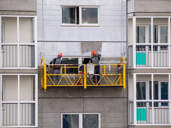 construction workers installers high-rise workers industrial climbers, painters on the lift paint the facade of the building, completion of construction of a residential building or office