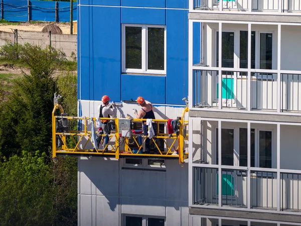 construction workers installers high-rise workers industrial climbers, painters on the lift paint the facade of the building, completion of construction of a residential building or office