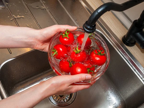 a woman\'s hand holds tomatoes under running tap water, the importance of handling and thoroughly washing vegetables and fruits during the covid-19 coronavirus pandemic