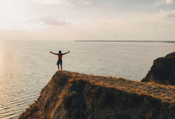 a man stands with his hands up on a hill by the sea