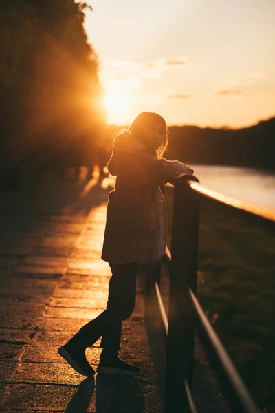 En liten flicka på bron. bakgrund av floden och solnedgång Stockfoto