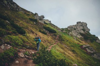 Sırt çantalı bir yürüyüşçü, Karpatlar 'ın yeşil dağları arasında yol boyunca yürür. Ortalama planın arkasındaki fotoğraf.