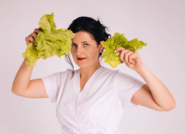 Bornozlu kadın beslenme uzmanı ve beyaz arka planda farklı sebzeler.
