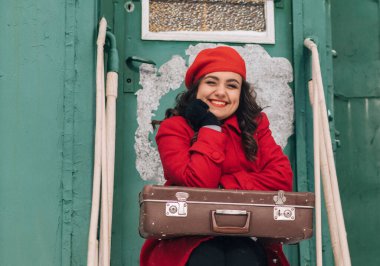 Trenin yanındaki tren istasyonunda bavullu kırmızı elbiseli kız. 