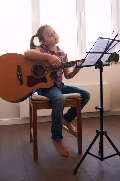 A little girl learns to play the guitar from notes. Music school for children.Musical notation. — Stock Photo, Image