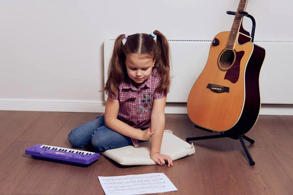 Una niña aprende a tocar la guitarra de las notas. Escuela de música para niños.Notación musical. —  Fotos de Stock