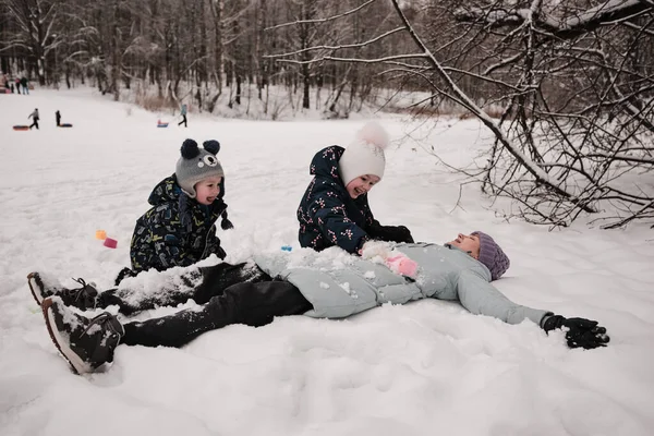 Copiii cu mama lor zac în zăpadă. Copiii își acoperă mama cu zăpadă și râd — Fotografie, imagine de stoc