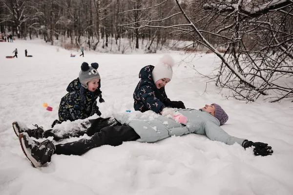 Les enfants avec leur mère sont couchés dans la neige. Les enfants couvrent leur mère de neige et rient Photos De Stock Libres De Droits