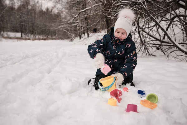 Uma criança brinca na neve com brinquedos de areia Imagem De Stock