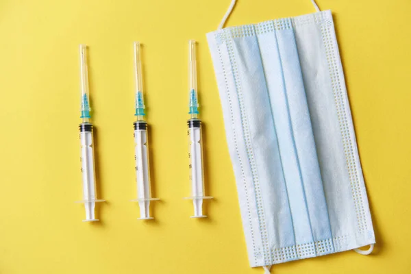 three syringes, a medical dressing, and vials for injecting the vaccine on a yellow background.