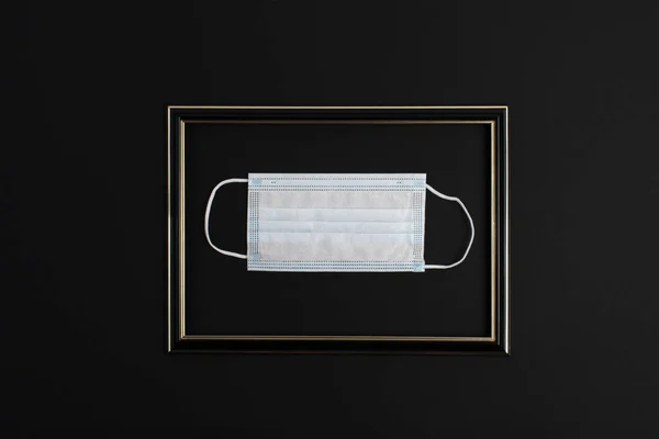Flat lay medical mask in a frame on a black background as an exhibit in a museum. Capture 2020 in one photo