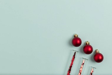 İçinde kırmızı parıltılar olan tıbbi test tüpleri nane yeşili arka planda Noel toplarının yanında yatar. Festive flat with copy space