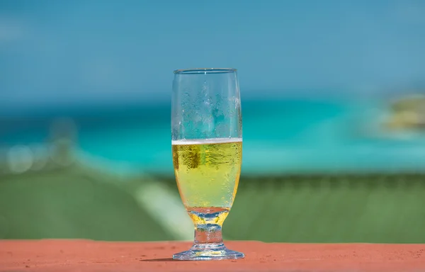 Vista de primer plano de medio vaso lleno con cerveza amarilla clara contra el océano y el fondo azul del cielo —  Fotos de Stock