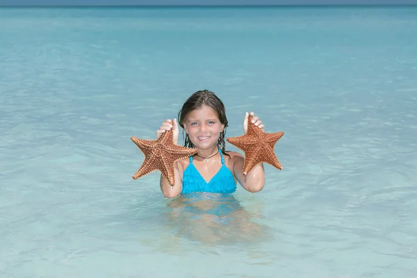 Joyful little girl caught two starfish in tranquil azure ocean — Stock Photo, Image