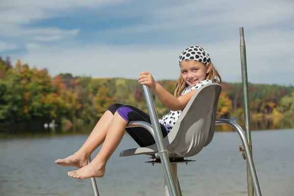 Fröhliches kleines Mädchen sitzt entspannt über dem Wasser im Rettungsschwimmstuhl vor herbstlichem Naturhintergrund — Stockfoto