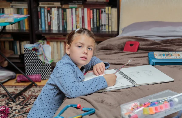 Kaunis muodikas pieni tyttö istuu hänen huoneessaan ja tekee kotitehtäviä — kuvapankkivalokuva