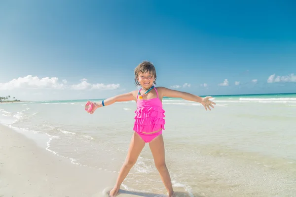 Szczęśliwy radosny uśmiechający się mała dziewczynka stojąc na plaży na jasny słoneczny dzień na tle niebo ocean i niebieski traquil — Zdjęcie stockowe