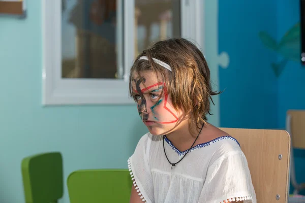 Unhappy serious, angry little girl with painted face sitting inside the kids room — Stock Photo, Image