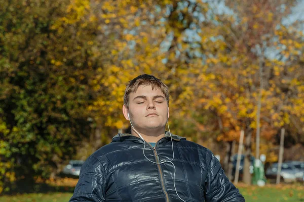 Teenage boy with  headphones listening the music in autumn park on sunny gorgeous warm day — Stock Photo, Image