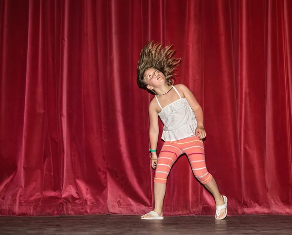 Mutlu, neşeli küçük kız göz saç hareketlerini o koşma, koyu kırmızı perdeler arka plan karşı gece sahnede dans ederken — Stok fotoğraf