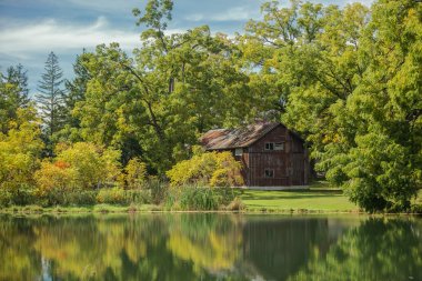 Amazing view of an  old vintage wooden abandoned cabin, standing in woods reflected in lake calm water on sunny warm autumn day clipart