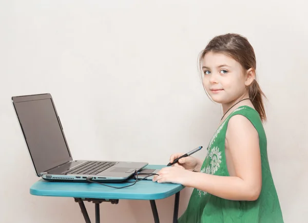 Довольно модная маленькая девочка сидит за столом и работает над своим ноутбуком — стоковое фото