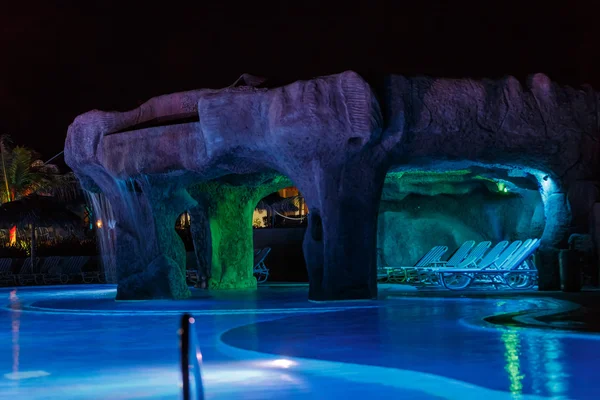 View of swimming pool with various colorful beautiful lights and cozy warm grotto — Stock Photo, Image