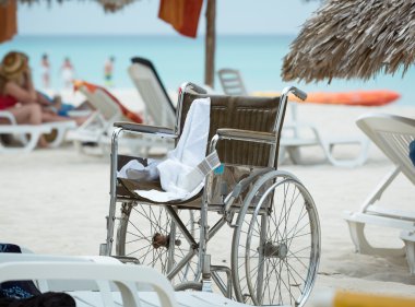 Empty wheelchair standing on tropical beach against ocean background clipart