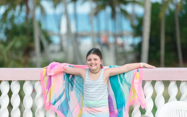 Feliz menina alegre em pé na varanda contra praia tropical e fundo do oceano — Fotografia de Stock