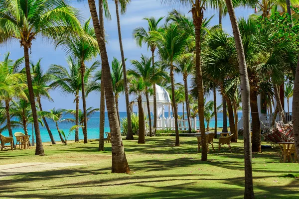 Fin utsikt över tropiska trädgård med vitt lusthus och lugnt hav bakgrund — Stockfoto