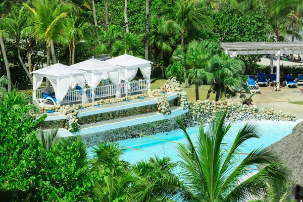 Grandes gazebos blancos cómodos cerca de la piscina en el jardín de palmeras tropicales — Foto de Stock