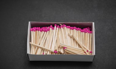 pink matchsticks in carton box on dark grey background clipart