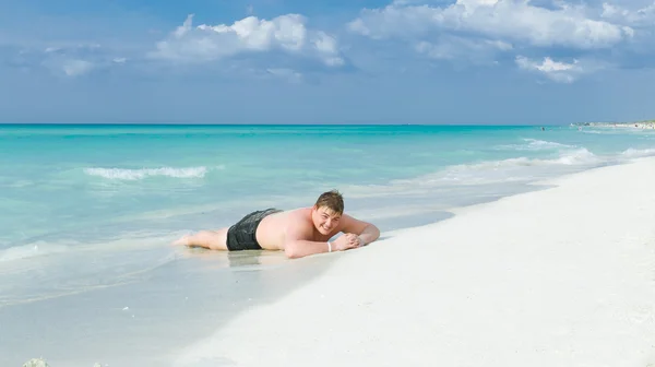 Happy, joyful teenage boy lying on white sand Cuban beach and enjoying his vacation time — Stock Photo, Image