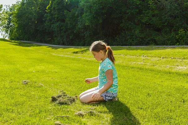 Девочка играет, смотрит вниз на зеленое травяное поле в солнечный день — стоковое фото