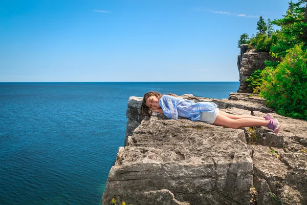 Happy, joyful little girl lying and relaxing on the edge of high cliff above gorgeous amazing Cyprus lake — Stock Photo, Image