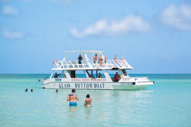 amazing beautiful tranquil turquoise ocean with people in background swimming and walking toward glass boat to get on board for traveling along the Cayo Coco, Cuban island