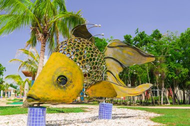 Giant big, decorative beutiful fish made of metal sheets and horshoe parts, standing on ceramic tile posts in cozy tropical garden clipart