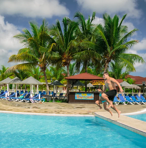 Bella vista incredibile del ragazzo e della bambina che giocano, saltando in piscina nella soleggiata giornata estiva nel giardino tropicale — Foto Stock