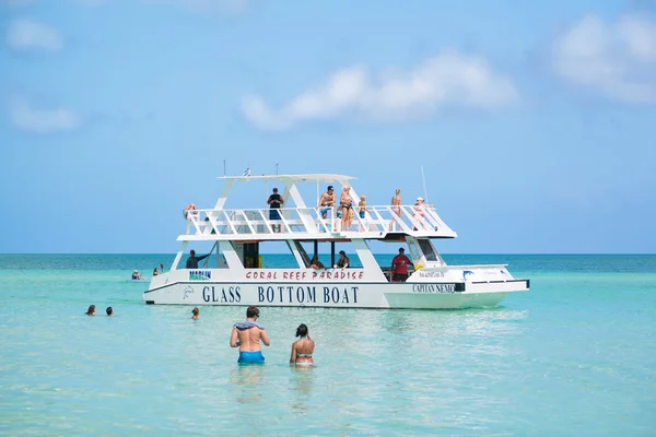 Asombroso hermoso océano turquesa tranquilo con gente en el fondo nadando y caminando hacia el barco de cristal para subir a bordo para viajar a lo largo del Cayo Coco, isla cubana — Foto de Stock