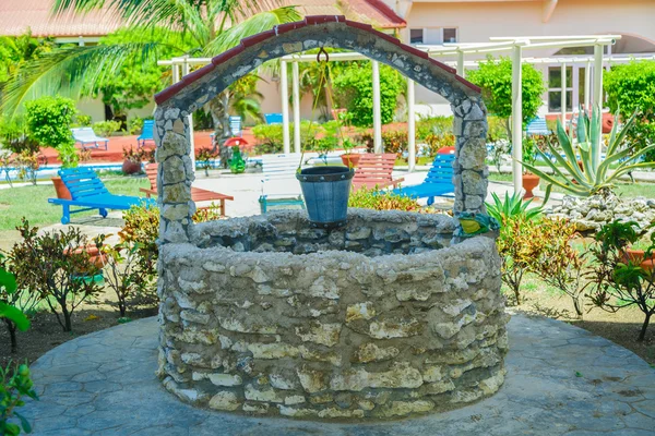 Old natural vintage stone will with pail standing in outdoor spa tropical garden grounds — Stok fotoğraf