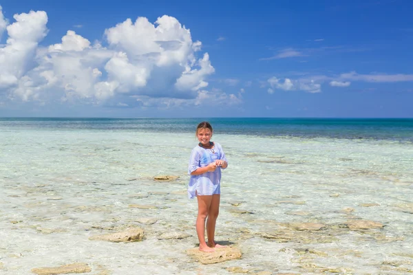 Smilling joyful happy little girl standing on a small stone in the ocean on sunny gorgeous day — Stok fotoğraf