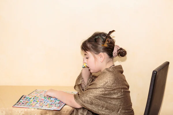 Красивая маленькая девочка сидит за столом и учится, читает книгу — стоковое фото