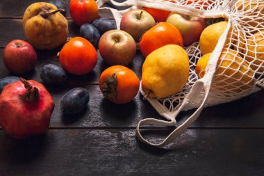 Koyu ahşap arka planda ağlı bir çantada çeşitli sonbahar meyveleri..